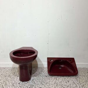 Burgundy back to wall toilet pan and small basin with white backdrop and bathroom tiles