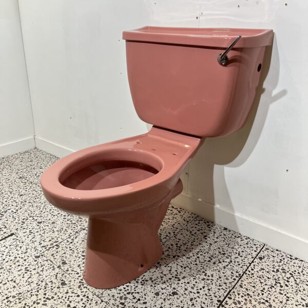 Pink close coupled toilet with white background and retro tiles