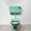 Turquoise low level toilet pan and cistern on white backdrop with bathroom tiles