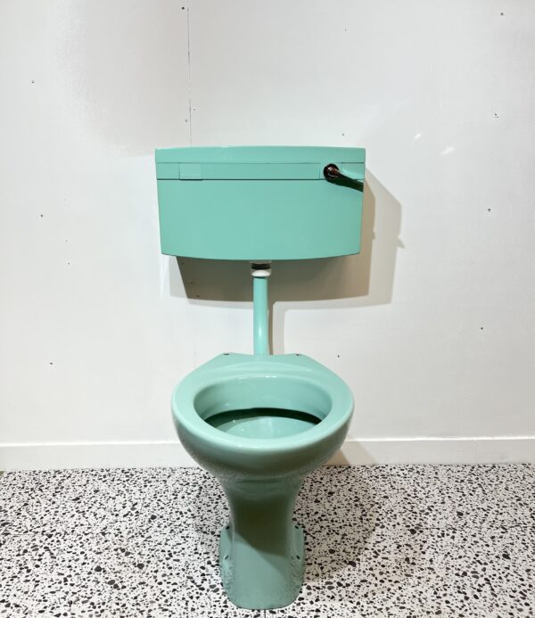 Turquoise low level toilet pan and cistern on white backdrop with bathroom tiles