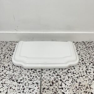 White traditional style toilet cistern lid with white backdrop and bathroom tiles