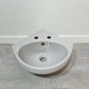 light grey corner basin with 2 tap holes on white back drop and grey bathroom tiles