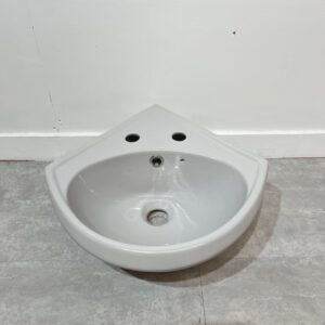 light grey corner basin with 2 tap holes on white back drop and grey bathroom tiles