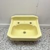 Small yellow hand wash basin made by Twyfords with 2 tap holes on white back drop with retro bathroom tiles