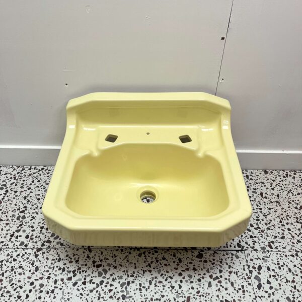 Small yellow hand wash basin made by Twyfords with 2 tap holes on white back drop with retro bathroom tiles