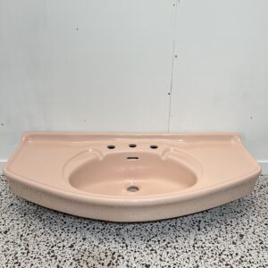 large pink retro basin with 3 tap holes on white backdrop and retro bathroom tiles