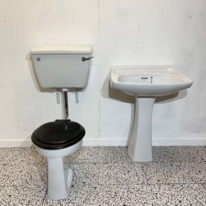 white low level toilet and sink with pedestal toilet has black seat with white backdrop and bathroom tiles