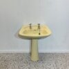 yellow ivorie de medici basin and pedestal made by ideal standard with chrome taps on white backdrop with bathroom tiles