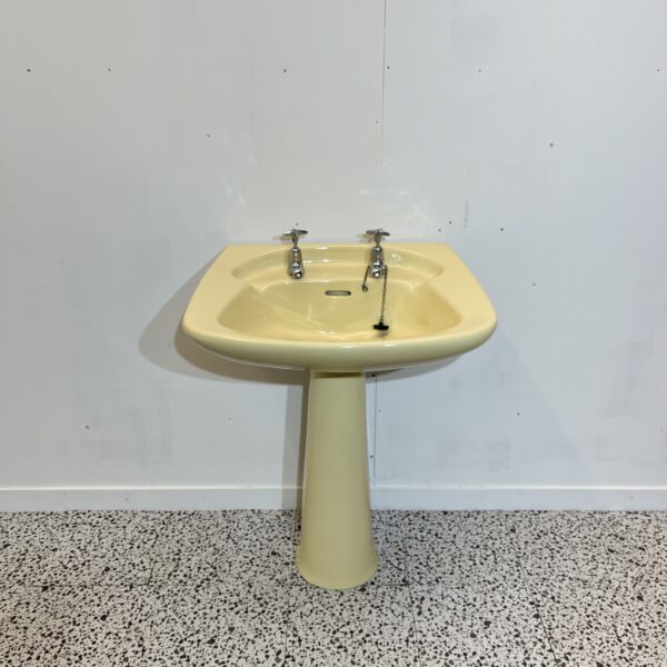 yellow ivorie de medici basin and pedestal made by ideal standard with chrome taps on white backdrop with bathroom tiles